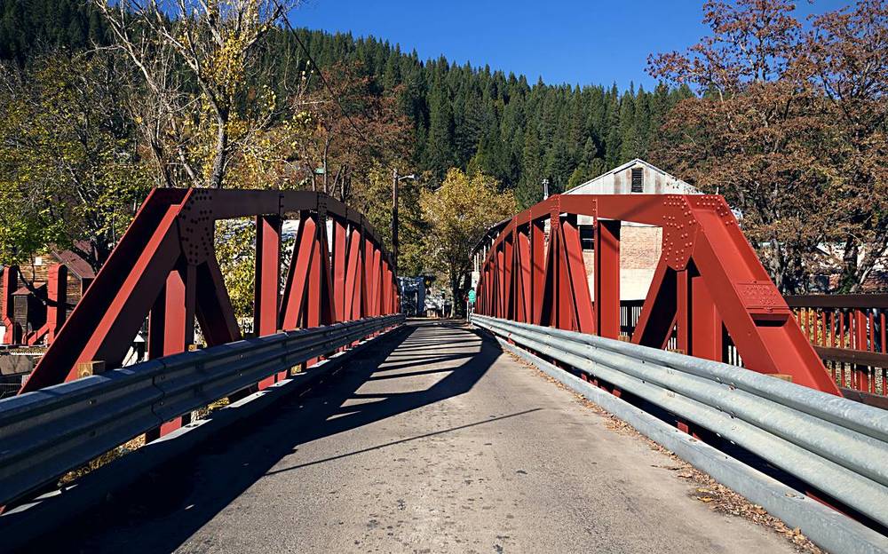 A red steel truss bridge over the Downie River in Downieville, California, with the forested canyon wall rising behind the town.