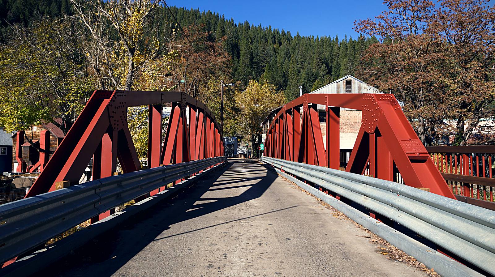 A red steel truss bridge over the Downie River leading into Downieville, California, with a forested canyon wall behind the town.